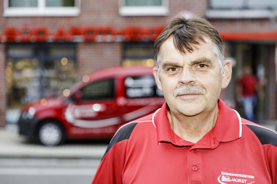 Mann schaut in die Kamera und trägt ein Rotes Arbeitshemd von Gesundheitszentrum Horst.
