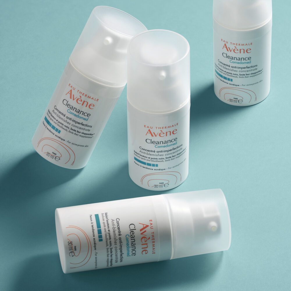 Vier weiße Pumpspender mit der Aufschrift Eau Thermale Avène Cleanance liegen und stehen auf einem türkisfarbenen Hintergrund, Produktlabels sind lesbar